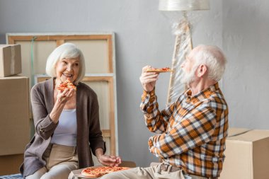 Yeni evde pizza yiyen ve arka planda karton kutular yiyen son sınıf çifti.