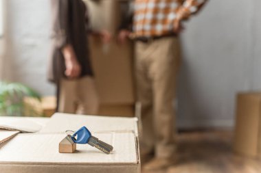 keys lying on cardboard box on foreground and blurred view of senior couple, moving concept clipart