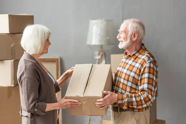 Senior Couple Holding Cardboard Box Looking Each Other New House — Stock Photo, Image