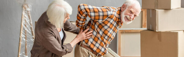 panoramic shot of senior man suffering from backache while wife trying help
