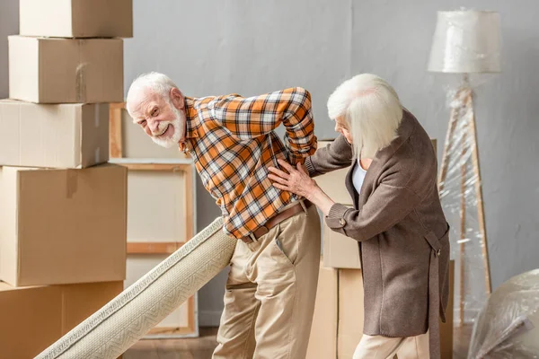 Senior Man Suffering Backache Holding Carpet While Wife Trying Help — Stock Photo, Image