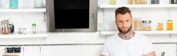 一个留着胡子 身穿白色T恤的男人站在网站上 看着厨房里的相机 — 图库照片