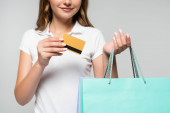 kivágott kilátás fiatal nő gazdaság hitelkártya és bevásárló táskák elszigetelt szürke, fekete péntek koncepció