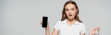 Gri ekranda boş ekranlı akıllı telefonu tutan şok olmuş kadının panoramik mahsulü 
