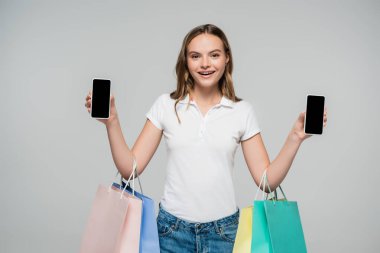 Elinde boş ekranlı akıllı telefonlar ve gri siyah cuma konseptine izole edilmiş alışveriş çantaları tutan neşeli bir kadın. 