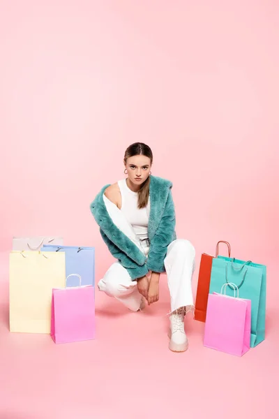 若い顧客は毛皮のジャケットピンクのショッピングバッグの近くに座っている黒い金曜日のコンセプト — ストック写真