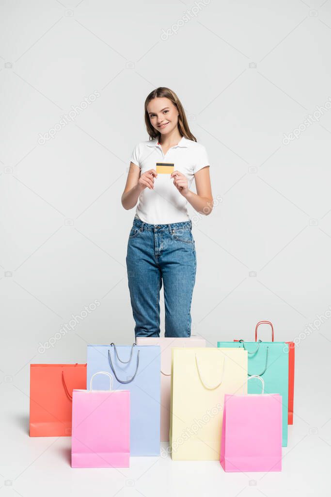 pleased young woman holding credit card near shopping bags on grey, black friday concept