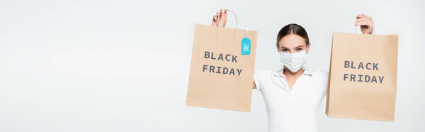 panoramic shot of customer in medical mask holding shopping bags with sale tag and black friday lettering isolated on white 