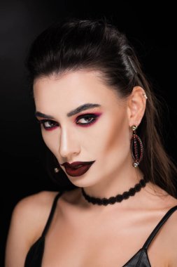Siyah makyajlı genç bir kadın siyah kameraya bakıyor.  