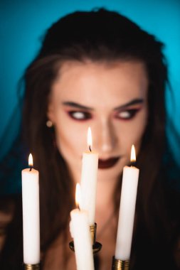 selective focus of burning candles near woman with black makeup on blue clipart