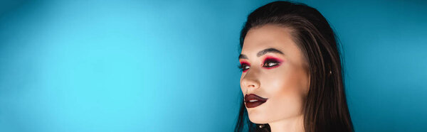 panoramic crop of young woman with dark makeup looking away on blue