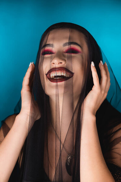 evil woman with black makeup, closed eyes and veil laughing on blue
