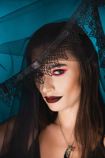 evil bride with makeup looking at camera through black veil on blue