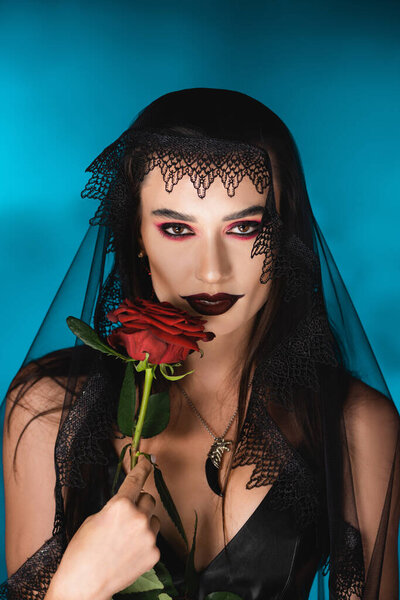 evil woman with black makeup and dark veil holding rose on blue