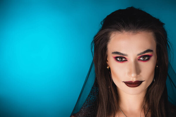 woman with black makeup and veil looking at camera on blue