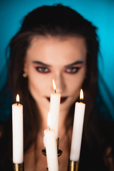 selective focus of burning candles near young woman with black makeup on blue