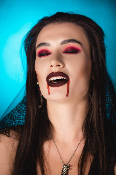 young woman in veil, with blood on face and closed eyes on blue