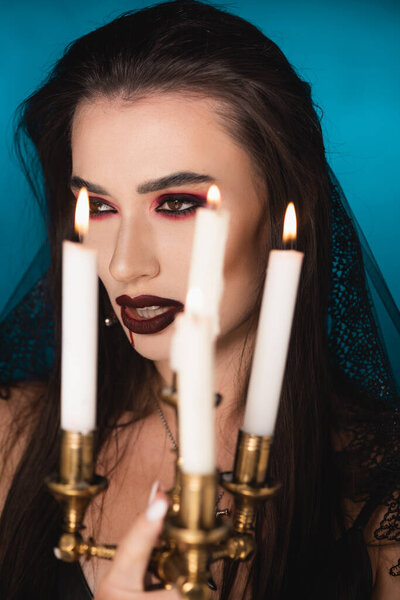 selective focus of woman in veil with blood on face near burning candles on blue