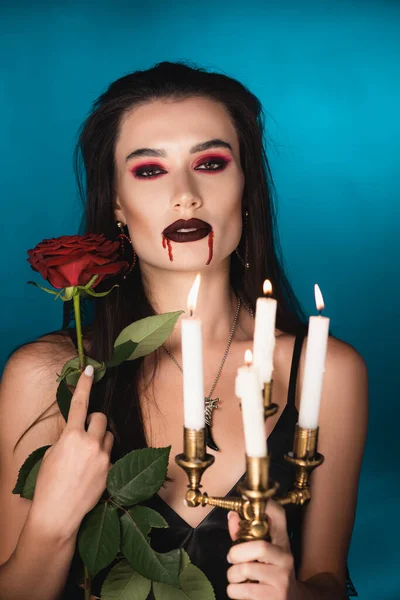 creepy woman with blood on face holding burning candles and red rose on blue
