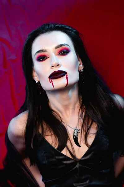 pale woman with blood on face looking at camera on red