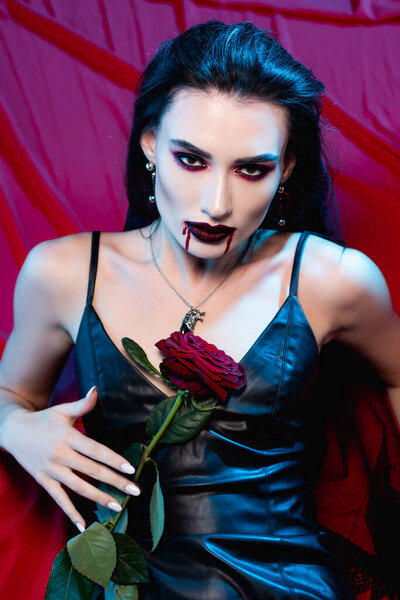 pale woman with blood on face looking at camera and holding rose on red