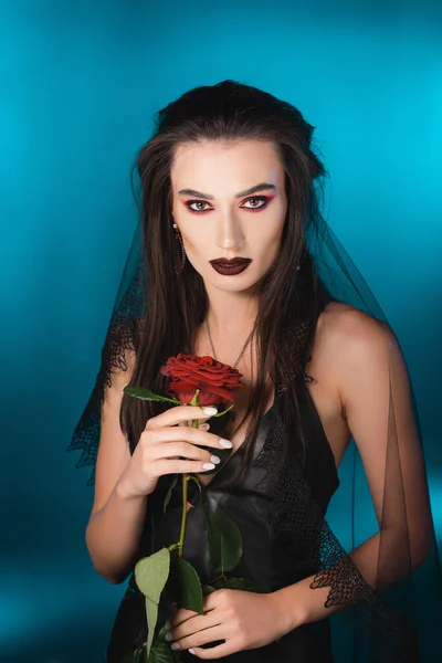 Joven Morena Con Maquillaje Oscuro Sosteniendo Rosa Roja Sobre Azul — Foto de Stock