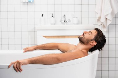 Sakallı adam evde gözleri kapalı banyo yapıyor.