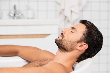 Sakallı adam evde gözleri kapalı banyo yapıyor. 