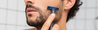 Cropped view of bearded man shaving with razor, banner  clipart