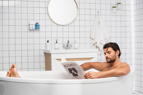 Bearded man with business lettering on newspaper taking bath at home 