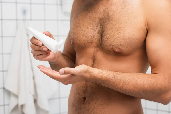Cropped view of shirtless man holding tube with cosmetic cream in bathroom