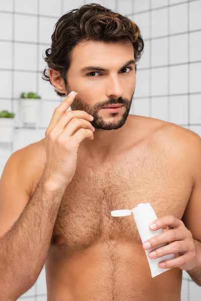 Hemdloser Mann Der Kosmetikcreme Aufträgt Und Badezimmer Die Kamera Schaut — Stockfoto