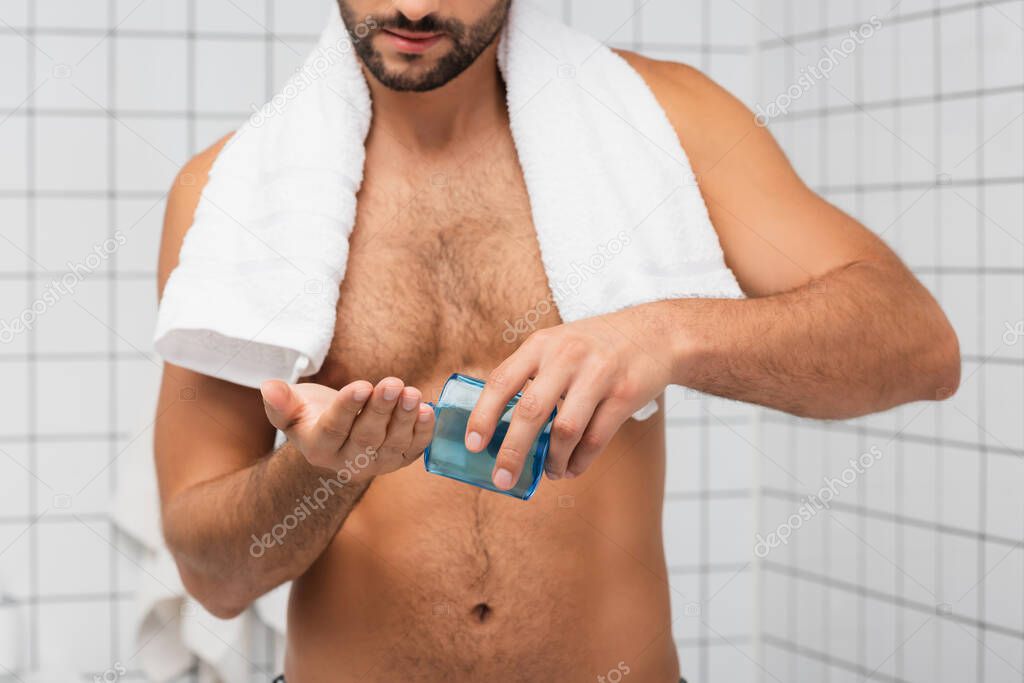 Cropped view of shirtless man with towel pouring after shaving lotion in bathroom 