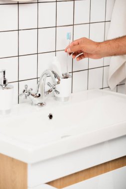 Tuvaletteki lavabonun yanındaki diş fırçasından diş fırçası alan adam görüntüsü. 