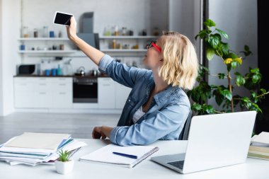 Genç sarışın kadın evde çalışırken selfie çekiyor.