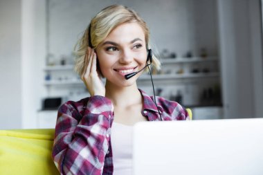 Kareli gömlekli ve kulaklıklı genç sarışın kadın online konferans yapıyor.
