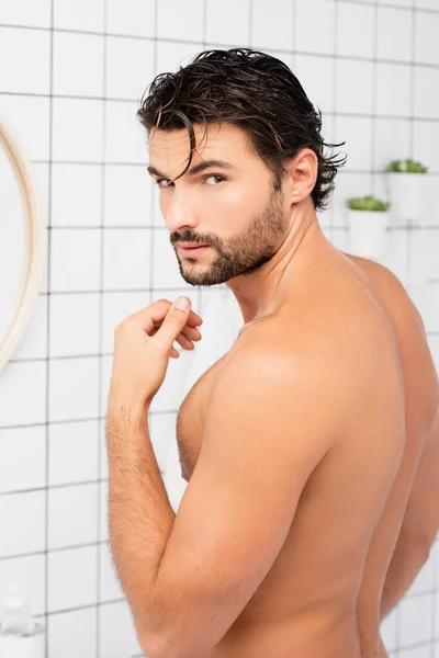 Muscular man with wet hair looking at camera in bathroom
