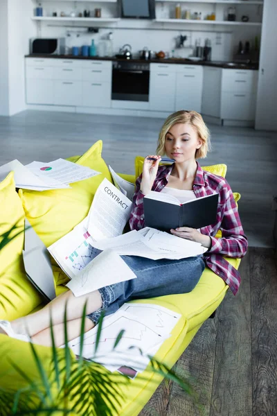 Young Blonde Woman Checkered Shirt Lying Sofa Documents Holding Notebook — Stock Photo, Image