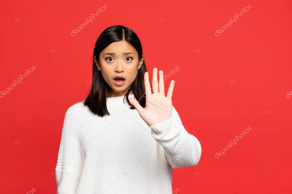 shocked asian woman with open mouth showing stop sign with palm isolated on red 