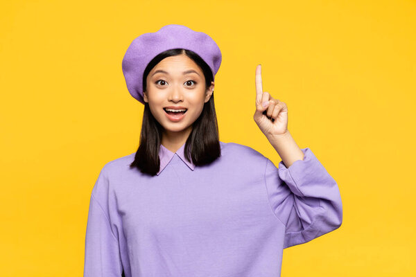 счастливая азиатка в берете указывает пальцем на желтый 