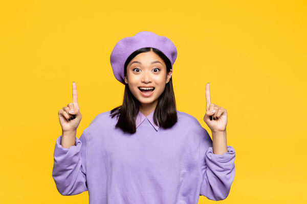 счастливая азиатка в берете указывает пальцами на желтый