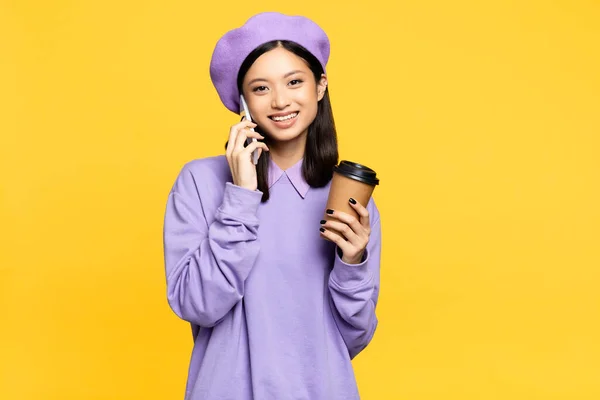 Happy Asian Woman Beret Holding Coffee Talking Smartphone Isolated Yellow — Stock Photo, Image