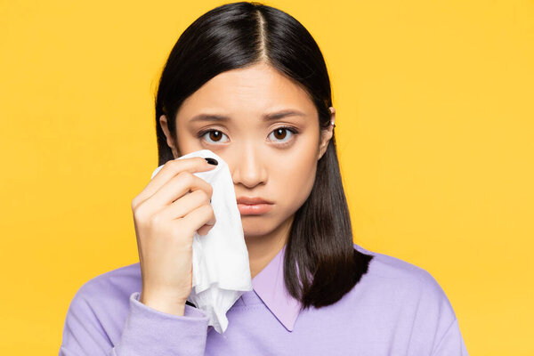 sad asian woman holding napkin while crying isolated on yellow 
