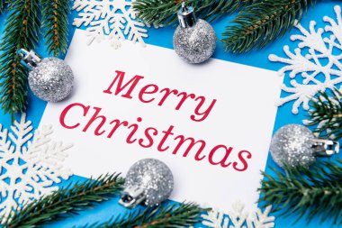 Kar tanelerinin üst manzarası, gümüş mücevherler ve ladin mavi arka planda mutlu bir Noel kartı.