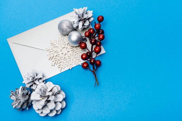 вид сверху на снежинку, серебряные безделушки, ягоды и конверт на голубом фоне