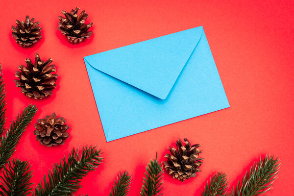 top view of cones, spruce branches and blue envelope on red background