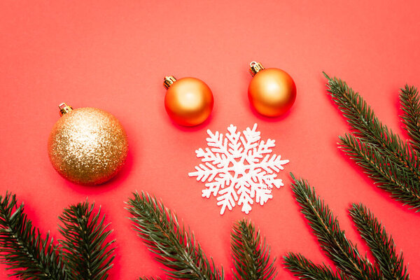 top view of snowflake, golden baubles and fir branches on red background
