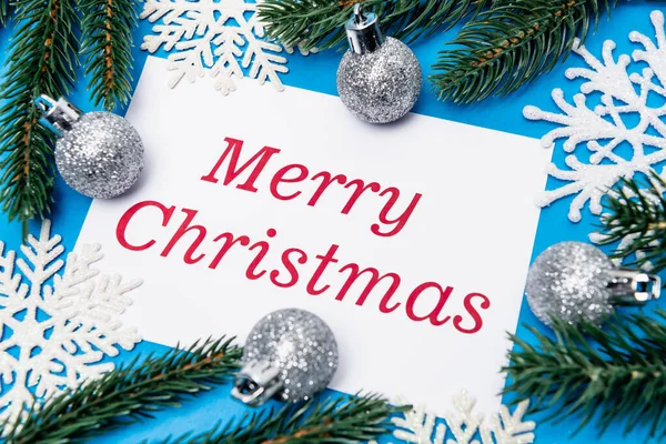 Top view of snowflakes, silver baubles and spruce with merry Christmas card on blue background — Stock Image Top View Snowflakes Silver Baubles Spruce Merry Christmas Card Blue Stock Photo