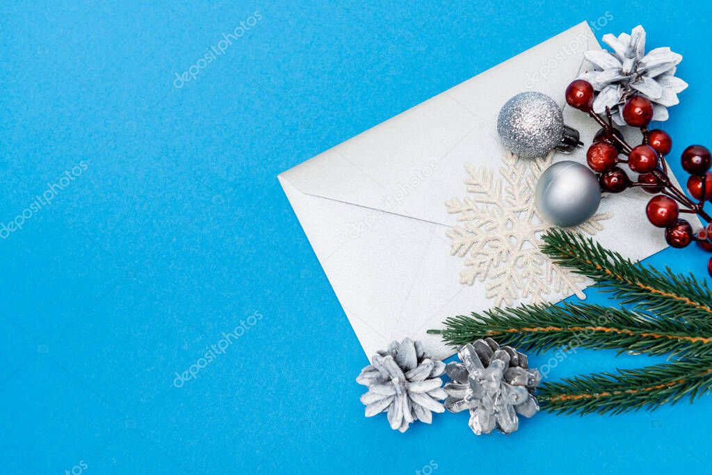 top view of snowflake, silver baubles, berries, spruce and envelope on blue background