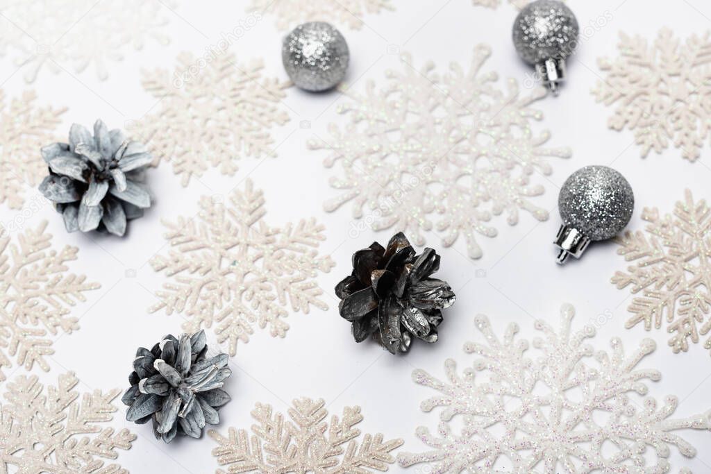 top view of snowflakes, silver baubles and cones on white background